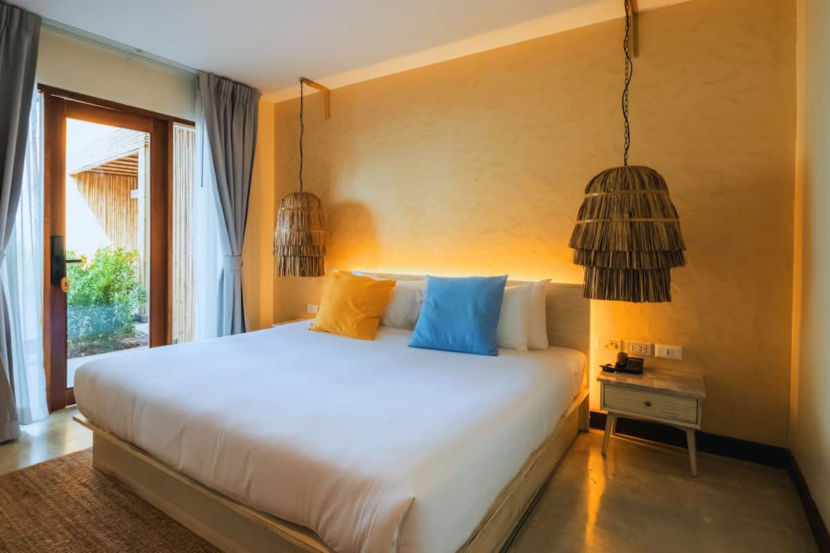 A hotel room with a large bed, two bedside lamps, a nightstand, and a view of the outdoors.