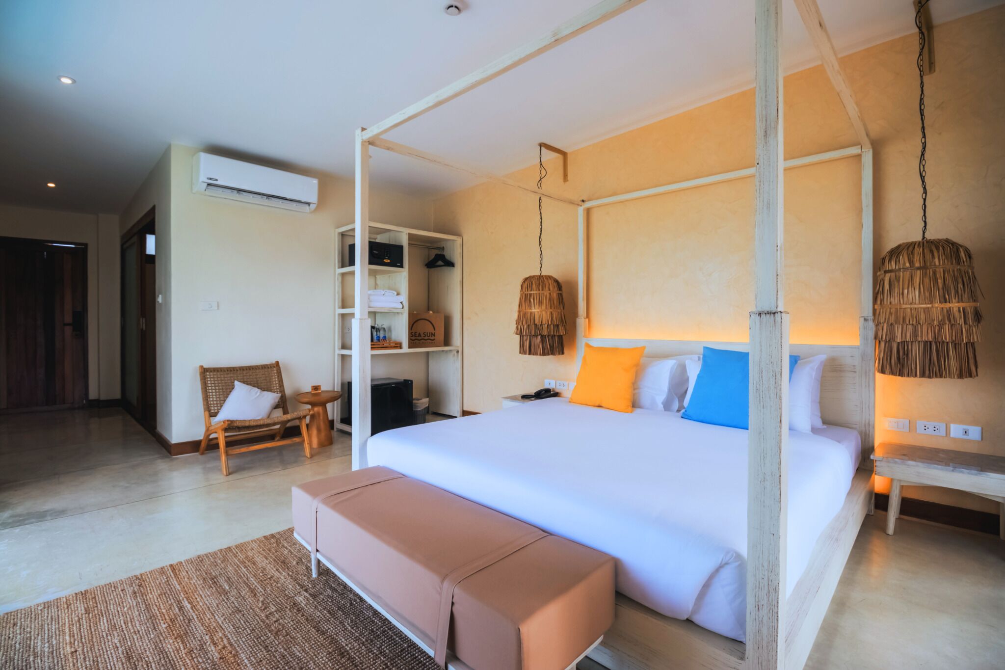 A spacious bedroom with a four-poster bed, a wooden bench, a wicker lamp, and a built-in wardrobe.