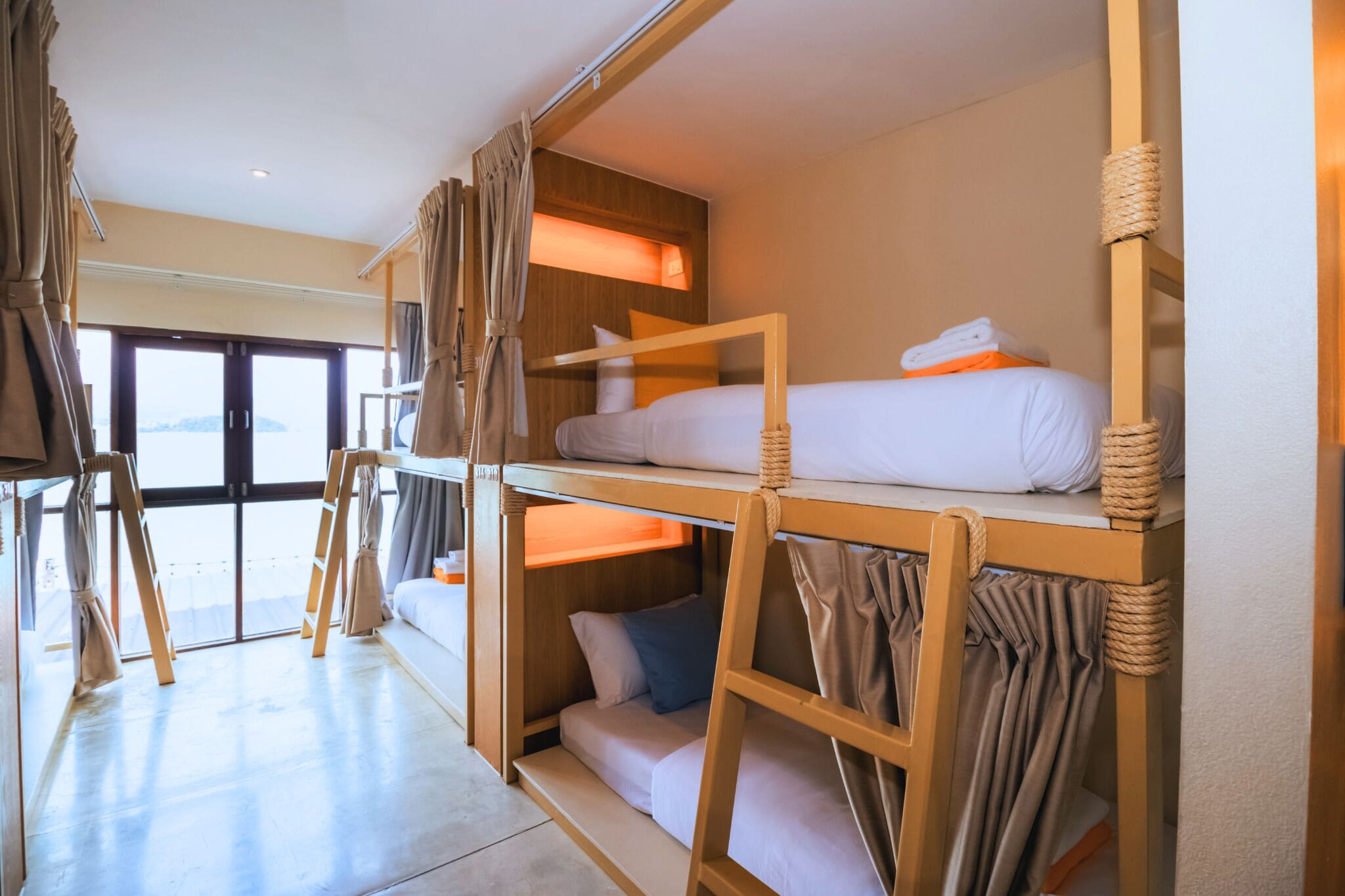 A bunk bed room with curtains, a window, and a view of the sea.