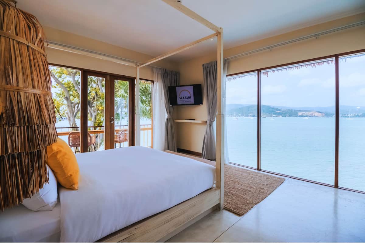 A bedroom with a large bed, a TV on the wall, and a view of the sea.
