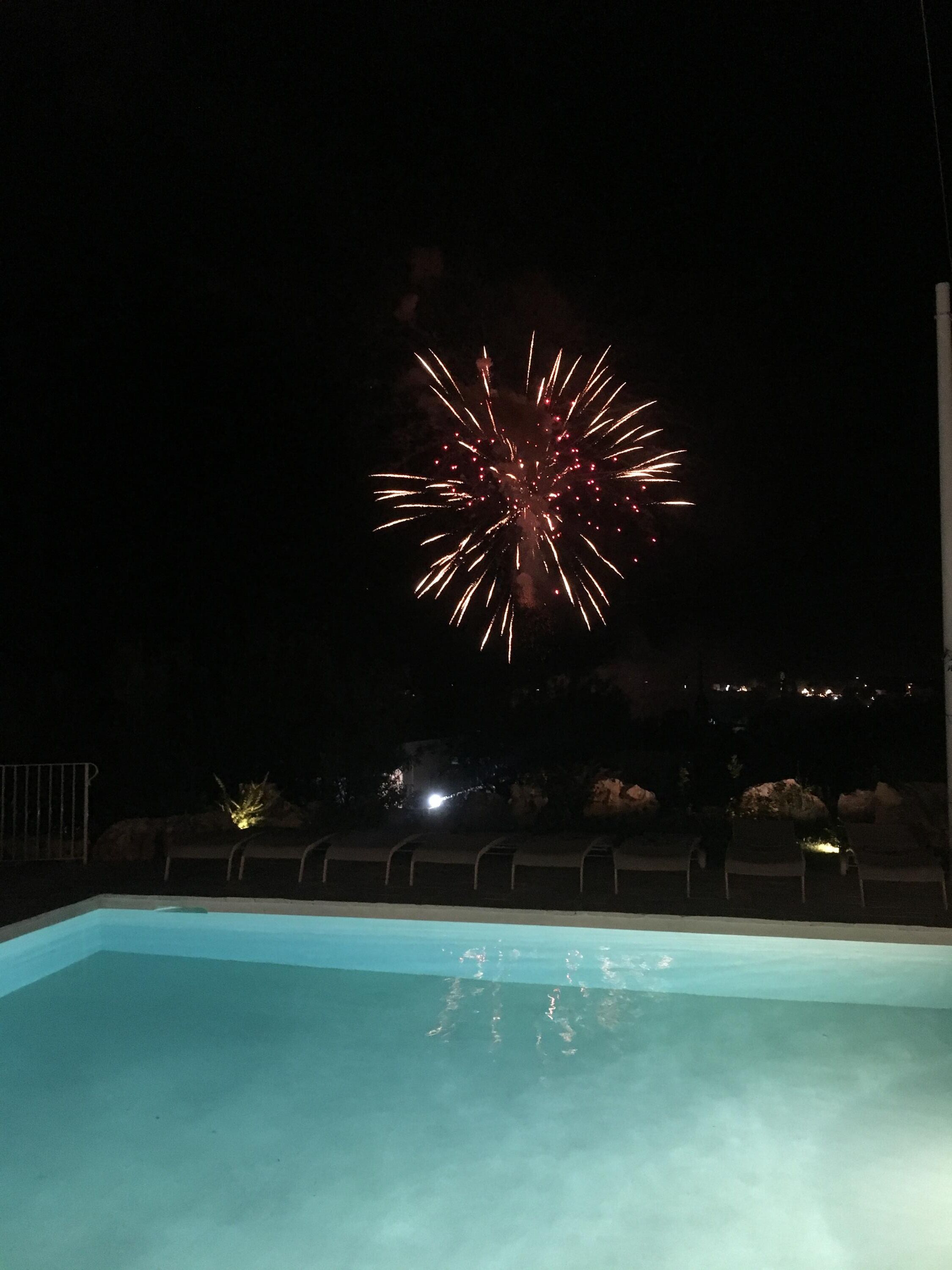 A swimming pool with a view of fireworks in the night sky.