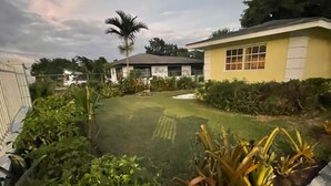 Un quartier résidentiel comprenant une maison, une cour clôturée et diverses plantes.