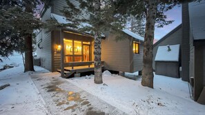 Eine Hütte mit Veranda und Bank, umgeben von verschneitem Gelände und Bäumen.