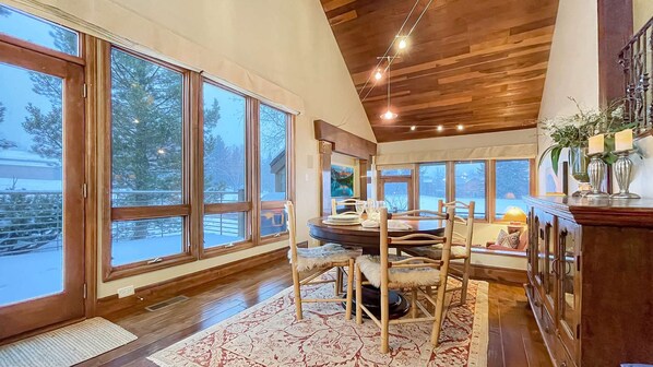 A dining area with a round table, chairs, and a view of a snowy landscape through large windows.