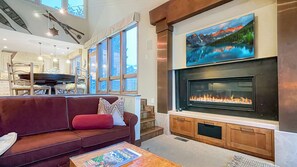 A modern living room with a fireplace, a large window, and a dining area. - Lakeside Retreat w/Views•Private Hot Tub•BBQ•Decks•Walk to Free Transit (Park City)