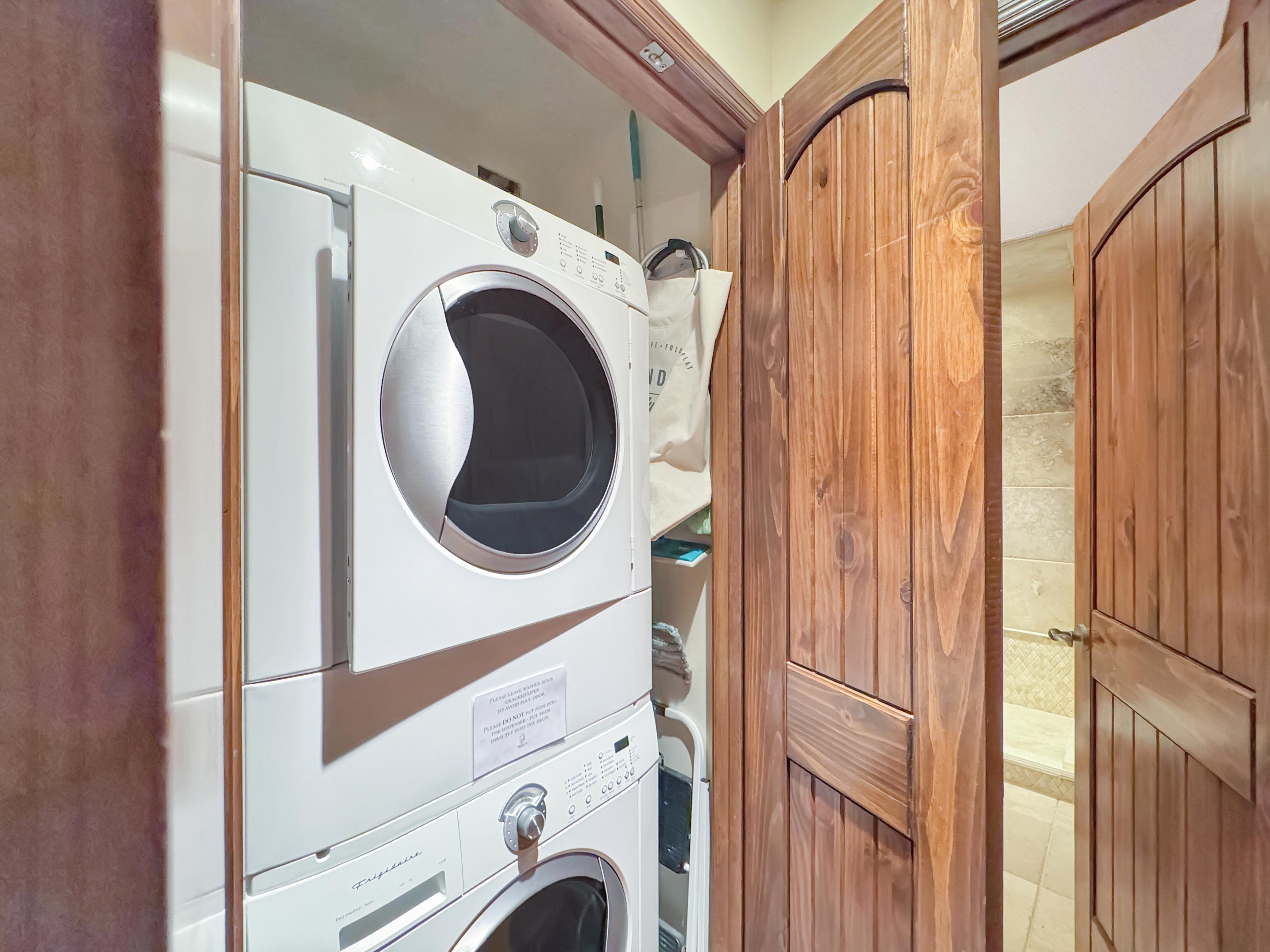 A laundry area with stacked washing machines and dryers, wooden doors, and a tiled wall.