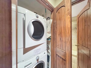 Een wasruimte met gestapelde wasmachines en drogers, houten deuren en een betegelde muur.