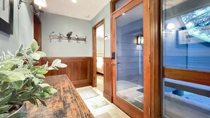 A wooden bench with a potted plant, a wall-mounted coat rack, and a sliding glass door leading to a covered outdoor area.