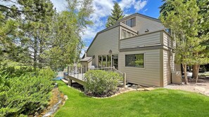 A two-story house with a deck, surrounded by trees and a small stream.