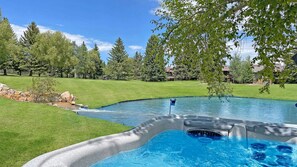 Een zwembad met een jacuzzi, omgeven door een verzorgd gazon en bomen.