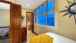 A bedroom with a bed, a window with blinds, a wooden door, and a wall-mounted decorative piece.