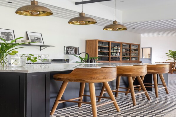 A modern kitchen with a central island, wooden bar stools, pendant lighting, and a checkered floor.