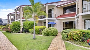 Un edificio residencial de varios pisos con balcones, un camino pavimentado y jardines bien cuidados.