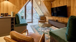 A cozy, modern living room with a sloped ceiling, wooden walls, a large TV, comfortable seating, and a view of a town through large windows. - Rooftop Vista Maisonette & Relaxing Bath by Interhome (Pec pod Snezkou)