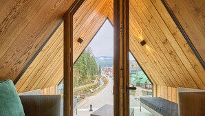 A high-ceilinged room with a large window, wicker furniture, and a view of a road and buildings. - Rooftop Vista Maisonette & Relaxing Bath by Interhome (Pec pod Snezkou)