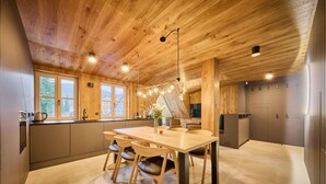 A modern kitchen with wooden ceiling, a dining table with chairs, and a large window. - Rooftop Vista Maisonette & Relaxing Bath by Interhome (Pec pod Snezkou)