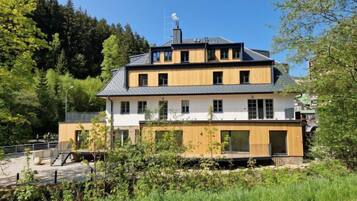 A two-story building with a modern design, featuring a combination of white and wooden exterior walls, large windows, and a sloped roof.