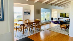 Ein modernes Wohnzimmer mit Essbereich, großen Fenstern und einem Fernseher.
