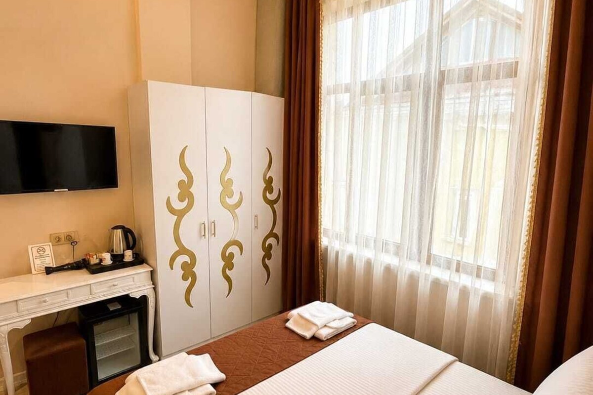 Una habitación de hotel con cama, escritorio, televisión y ventana con cortinas.