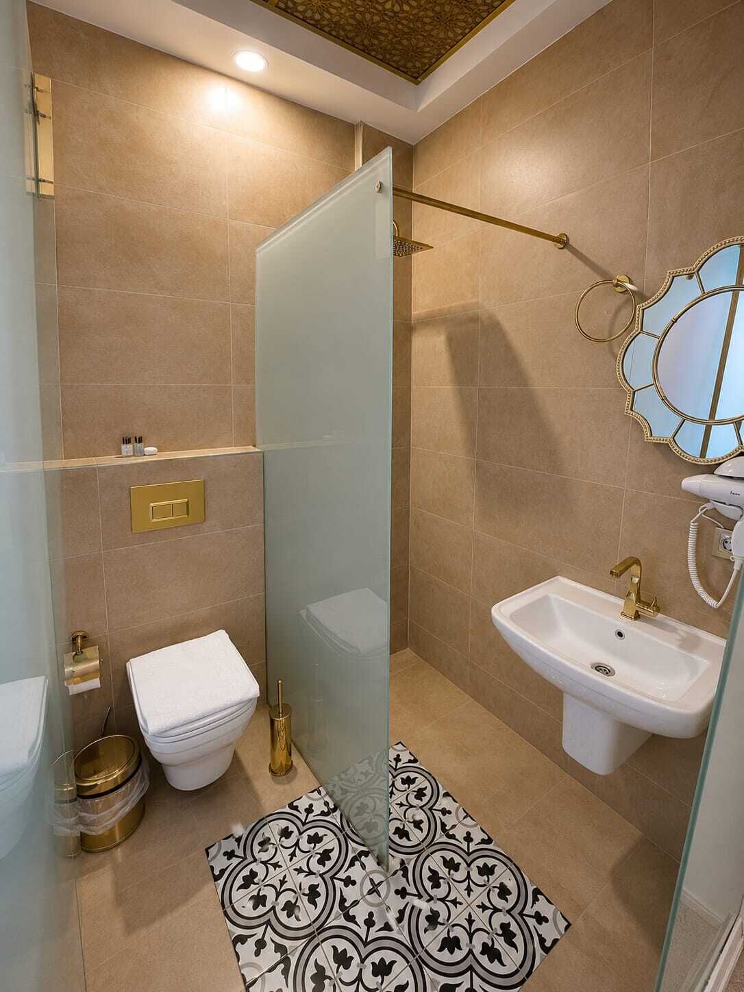 Un baño con cabina de ducha de vidrio, un lavamanos blanco y piso estampado.