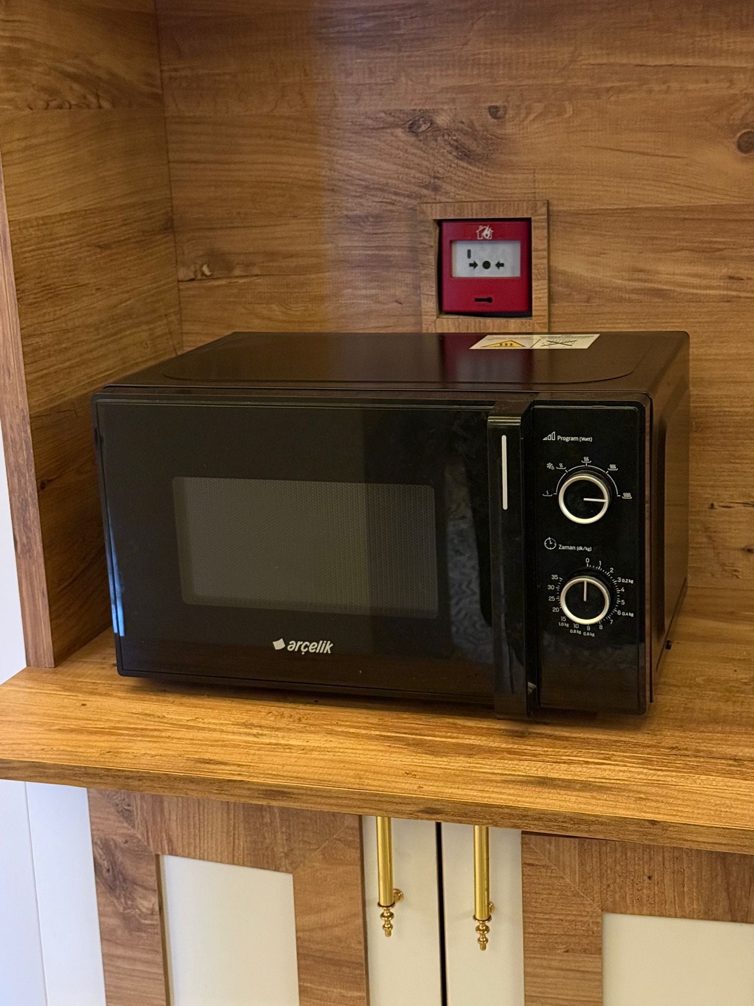 Eine schwarze Mikrowelle mit digitaler Anzeige und Bedienfeld, platziert auf einem Holzregal.