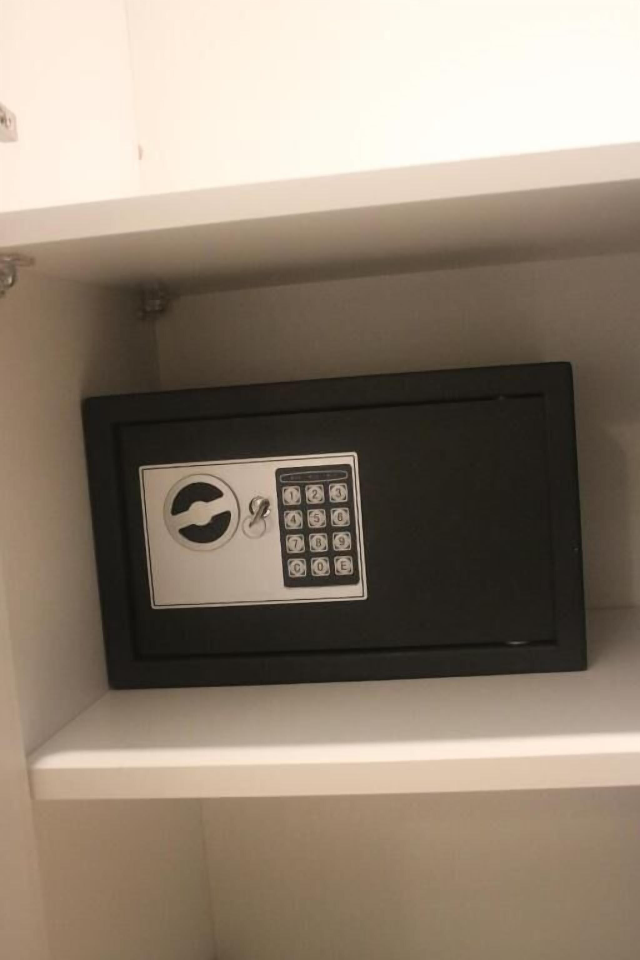 Um cofre preto com teclado e mecanismo de fechadura circular sobre uma prateleira branca.
