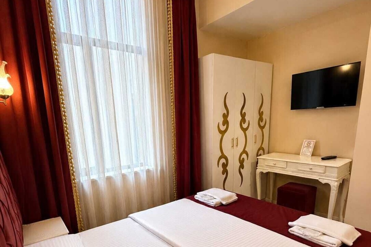 Habitación de hotel con dos camas, un escritorio, un televisor y una ventana con cortinas.