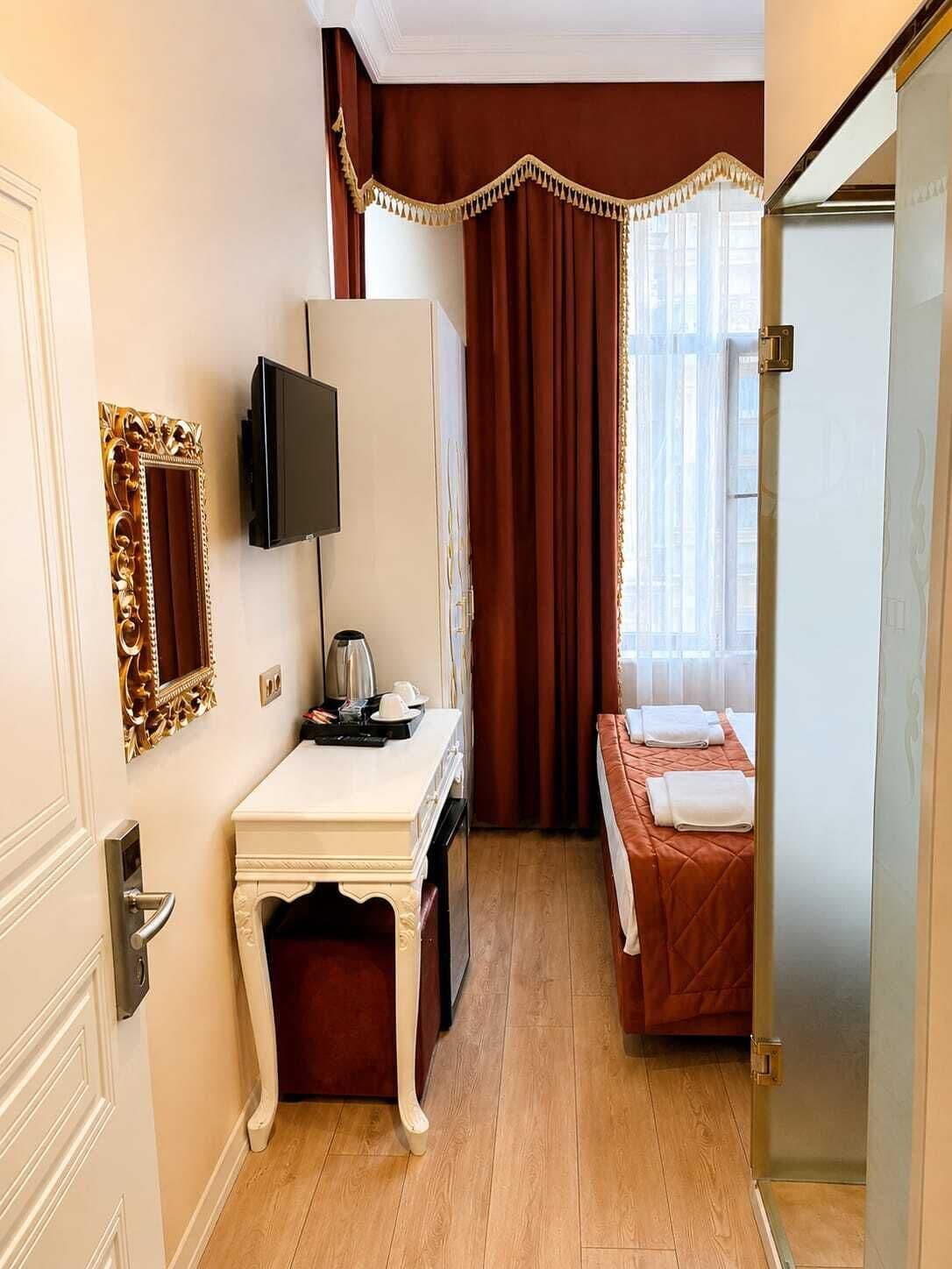 Una habitación de hotel con escritorio, televisor, cama y ventana con cortinas.