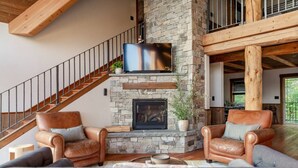 A spacious living room with a stone fireplace, leather sofas, and a wooden staircase. - Ponderosa Glen @ Ashley Lake (Kila)