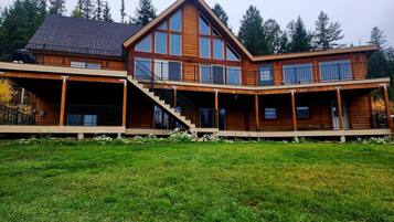 Ein zweistöckiges Holzhaus mit einer breiten Veranda, einer Garage und einer Treppe, die zum oberen Stockwerk führt.