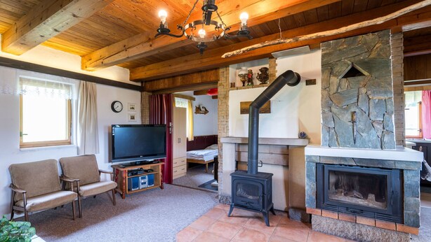 Ein gemütliches Wohnzimmer mit Kamin aus Stein, Holzbalkendecke und Fernseher auf einem Holzständer.