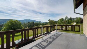 Ein Balkon mit Blick auf eine grüne Landschaft, eine gepflasterte Fläche und ein in der Nähe geparktes Auto.