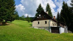 Ein zweistöckiges Haus mit Balkon, umgeben von Bäumen und einem grasbewachsenen Hügel.