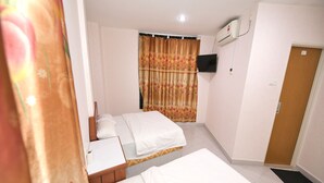 A hotel room with two beds, a desk, a TV, and an air conditioning unit.