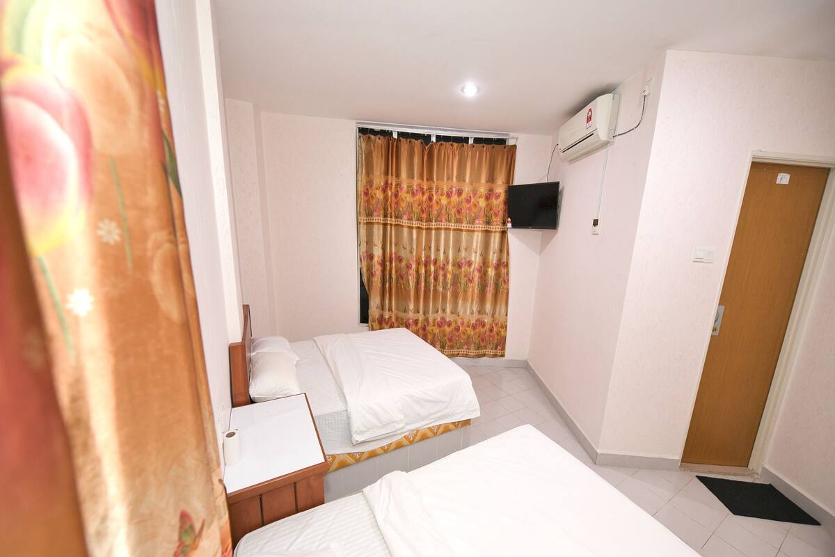 Ein Hotelzimmer mit zwei Betten, einem Schreibtisch, einem Fernseher und einer Klimaanlage.