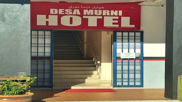The entrance to the Desa Murni Hotel with a red sign, a staircase, and a potted plant.