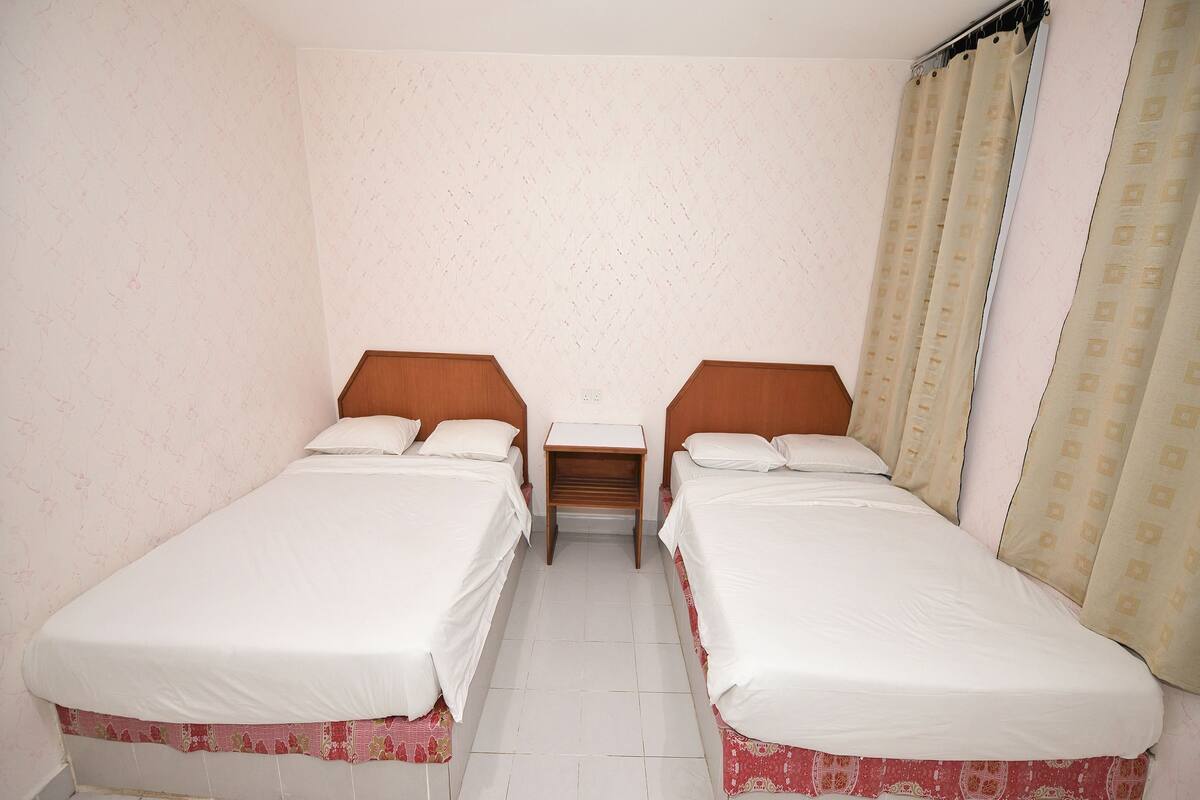 Ein Zimmer mit zwei Einzelbetten, einem Nachttisch und einem Vorhang.