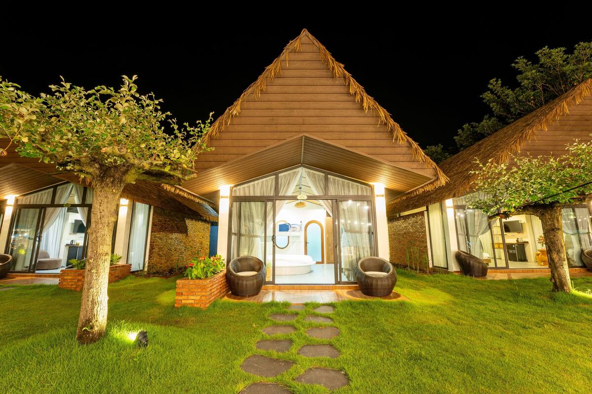 A two-story house with a thatched roof, a glass entrance, and a well-maintained lawn.