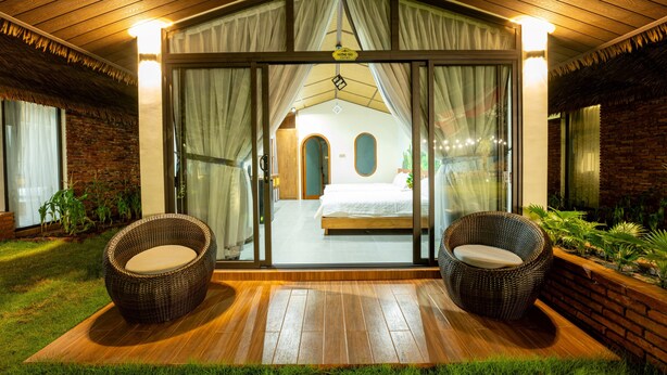 A hotel room with a large sliding glass door, a bed, and two wicker chairs outside. - Apple House & Coffee (Ho Chi Minh City)
