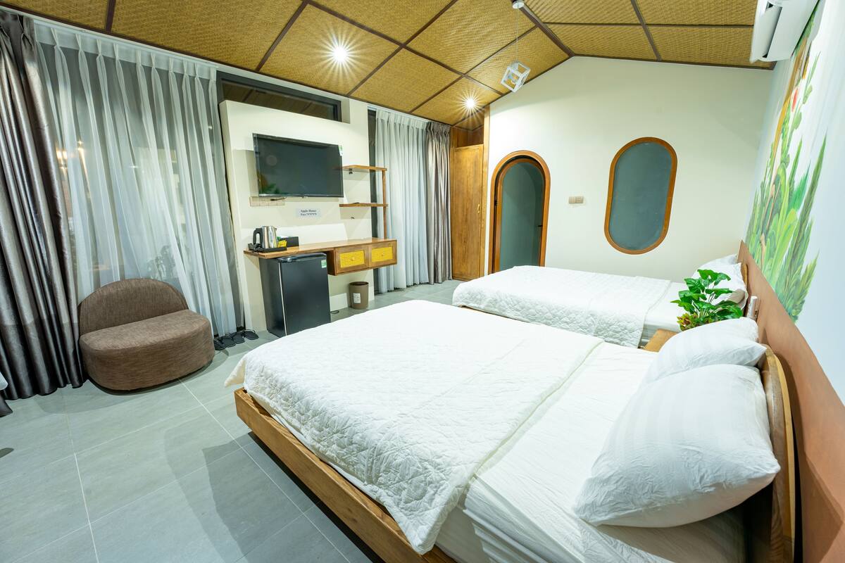 A hotel room with two beds, a desk, a chair, and a TV.