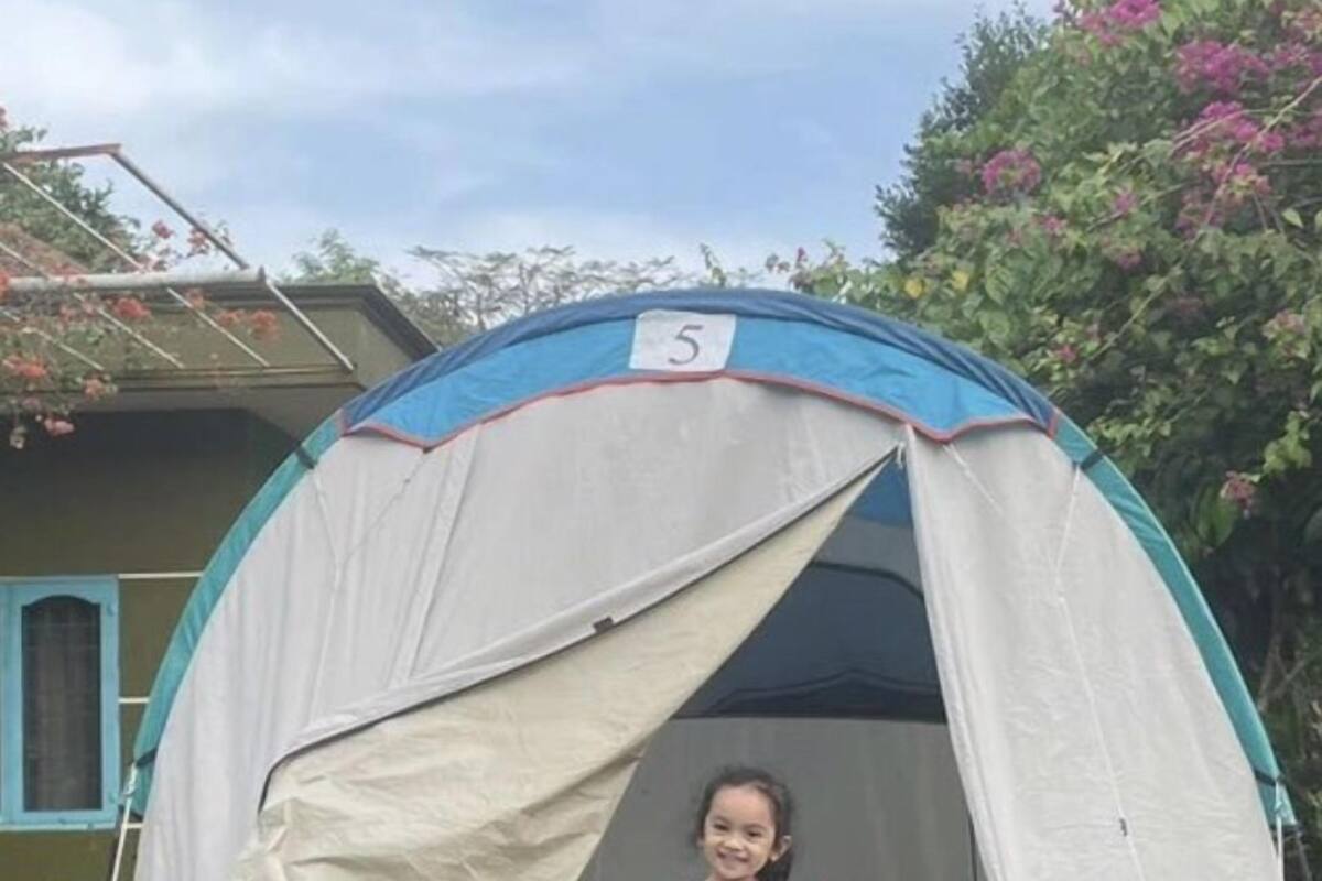 A tent with a number 5 on it, a young girl in a pink dress standing in front of it, and a fan inside the tent.