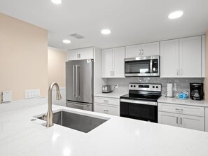 A modern kitchen with stainless steel appliances, white cabinetry, and a large island with a sink.