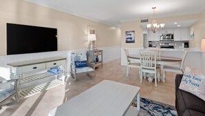 A modern living room with a flat-screen TV, a sofa, a coffee table, and a dining area with a table and chairs.