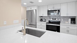 A modern kitchen with stainless steel appliances, white cabinetry, and a large island with a sink.