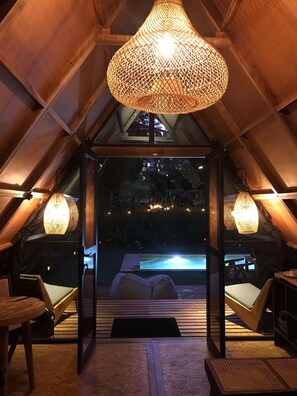Un ático acogedor y bien iluminado con una lámpara trenzada grande, asientos cómodos y vista a una piscina.