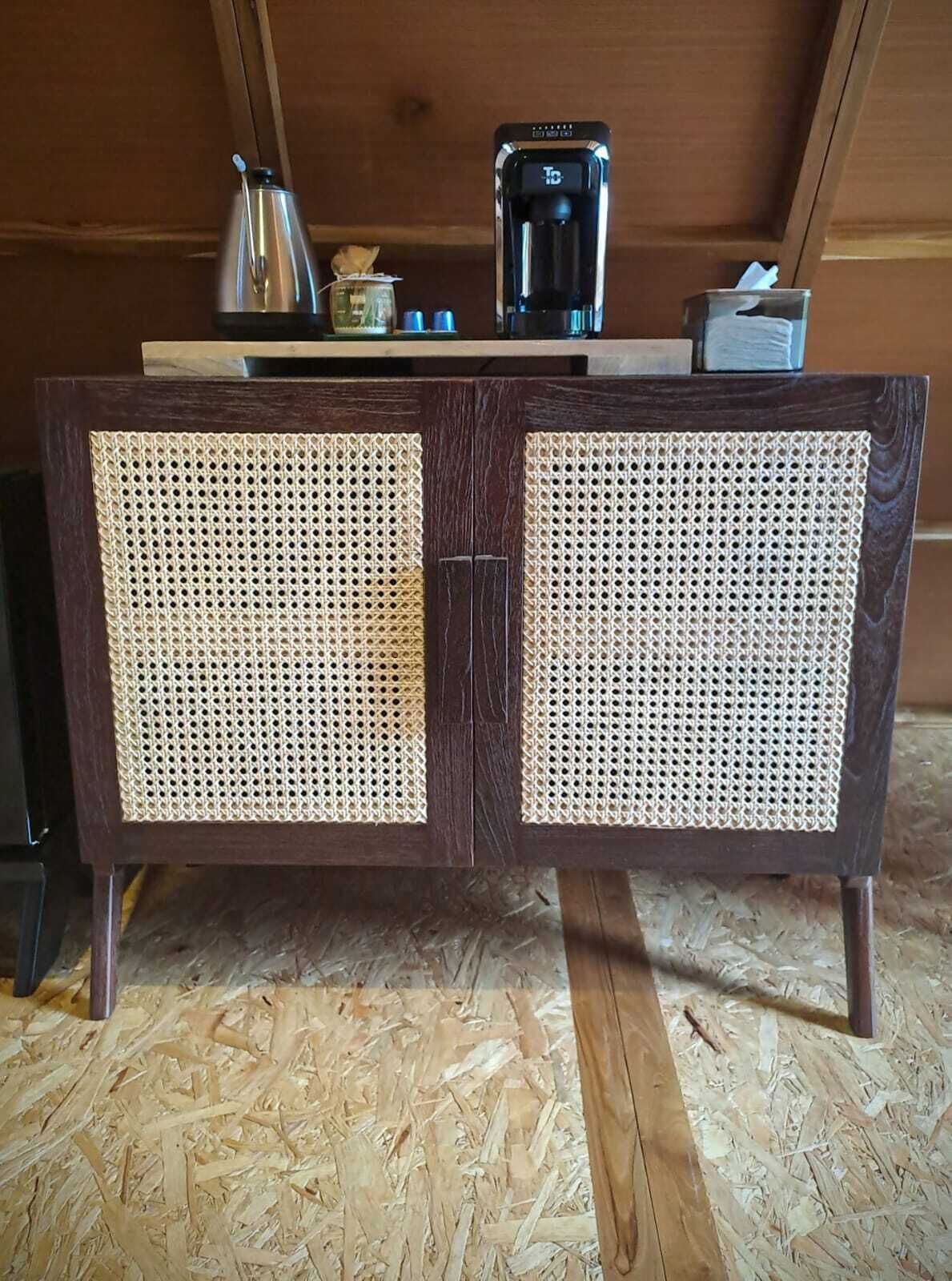 A wooden cabinet with woven panels, a coffee maker, and a glass container on top.
