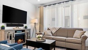 A living room with a flat-screen TV, a fireplace, a sofa, and a coffee table. - Downtown TC Condo | Rooftop + EV Charger Cornhole (Traverse City)