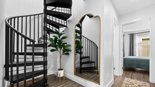 A modern interior with a spiral staircase, a large mirror, and a potted plant. - Downtown TC Condo | Rooftop + EV Charger Cornhole (Traverse City)