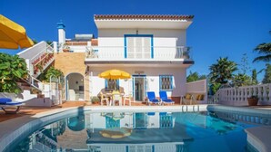 A two-story building with a swimming pool, a covered patio with chairs, and a staircase leading to the upper floor.