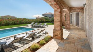 A poolside area with a brick archway, lounge chairs, and a clear view of the sea. - Vacation home Seseli by Interhome (Poreč/Sv. Lovreč)